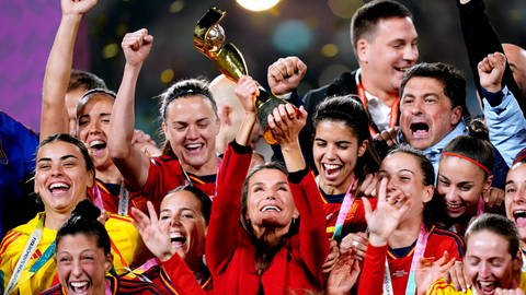 Königin Letizia von Spanien feiert mit dem spanischen Frauenfußballteam den WM-Sieg und hält den Pokal in den Händen.