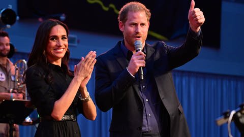 Prinz Harry von Großbritannien und seine Frau, Meghan, Herzogin von Sussex, stehen während der Invictus Games in Düsseldorf auf der Bühne. Beide nahmen an einem «Friends & Family»-Abendtermin der Spiele teil. Sie klatscht in die Hände und lacht, er zeigt mit dem Zeigefinger nach vorn.
