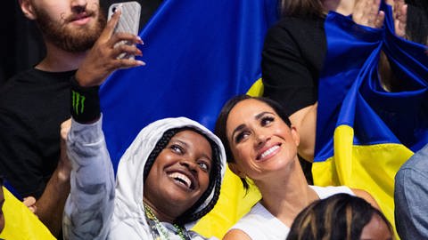 Meghan, Herzogin von Sussex, schaut sich bei den 6. Invictus Games in der Merkur Spiel-Arena zwischen Fans aus Nigeria und der Ukraine Sitzvolleyball der beiden Teams an und macht ein Selfie mit einem nigerianischen Fan. Der paralympische Wettbewerb für kriegsversehrte Sportler ist erstmals in Deutschland zu Gast.