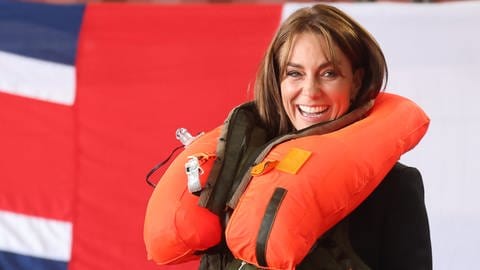 Prinzessin Kate lacht natürlich, nachdem sie bei einem Besuch der Royal Navy eine orangene Rettungsweste betätigt hat und diese sich geöffnet hat und schließlich voller Luft um ihren Hals liegt.