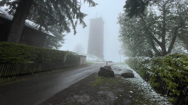 Nebel umgibt den Wasserturm von Dobel (Kreis Calw). Auf der Wiese ringsherum liegt Schnee. 
