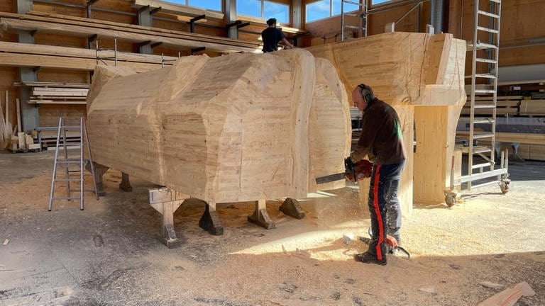 Ein Mann arbeitet mit der Motorsäge an einer Holzkuh.