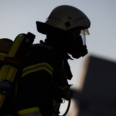Ein Feuerwehrmann in Atemschutzausrüstung steht an einem Einsatzfahrzeug der Feuerwehr. Ein Kind soll in einem Auto Feuerwerk angezündet und dadurch einen Brand auf der Autobahn 8 bei Stuttgart verursacht haben, teilt die Polizei mit.