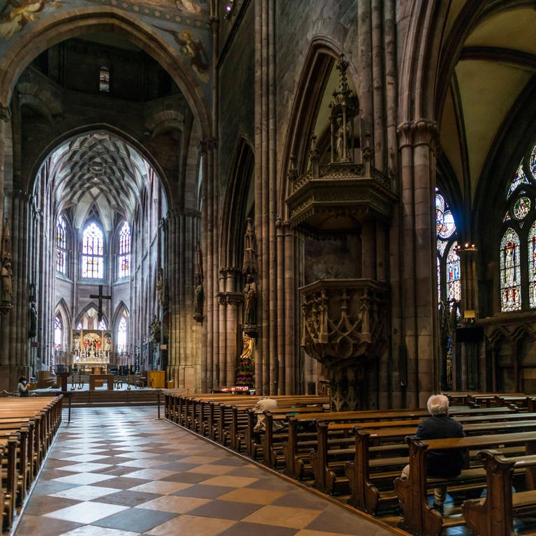 Der Kirchenraum des Freiburger Münsters, ein paar Gläubige sitzen auf den Bänken.