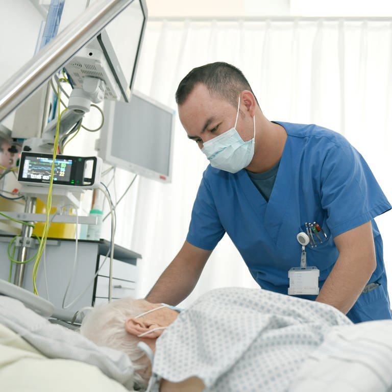 Ein Pfleger steht am Bett einer älteren Patientin in der Uniklinik Tübingen