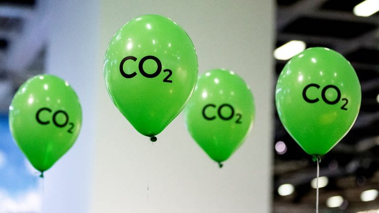 Grüne Luftballons mit der Aufschrift "CO2" schweben an einem Messesstand.