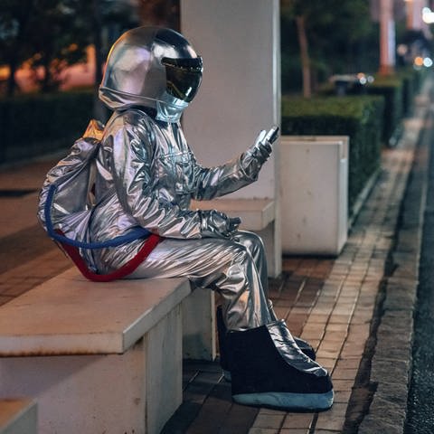 Eine als Astronaut verkleidete Person sitzt nachts an einer Bushaltestelle
